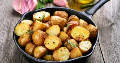Roasted potato in frying pan on wooden background